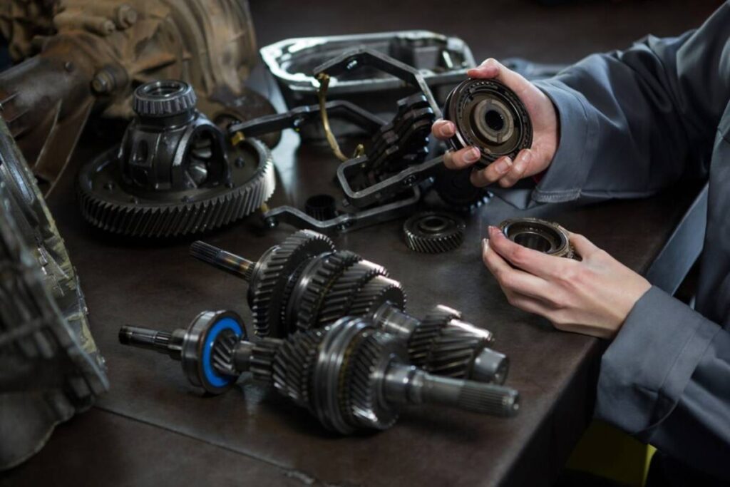 Hands assembling various mechanical parts, including gears and bearings, on a workbench in a workshop.
