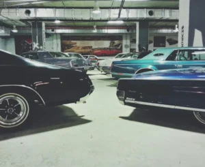 A collection of vintage cars in various colours, including black and blue, parked inside a spacious, industrial-style garage
