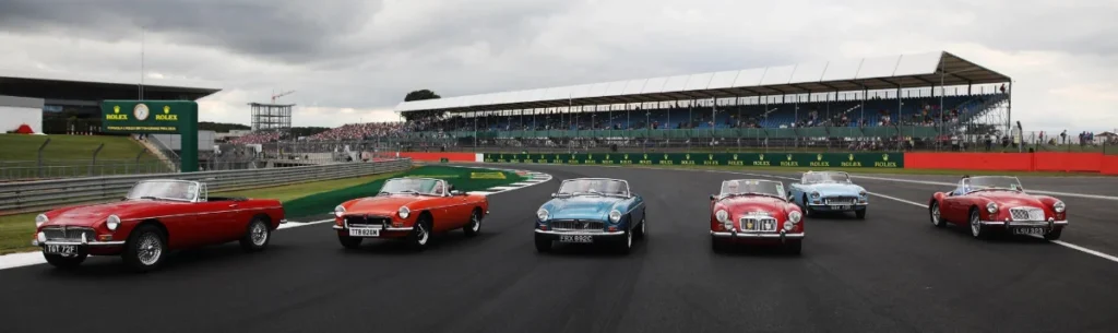 A panoramic view of five vintage sports cars racing on a track