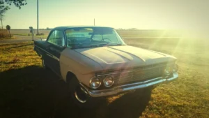 An old two-tone sedan parked in a rural area, under a golden sunlight