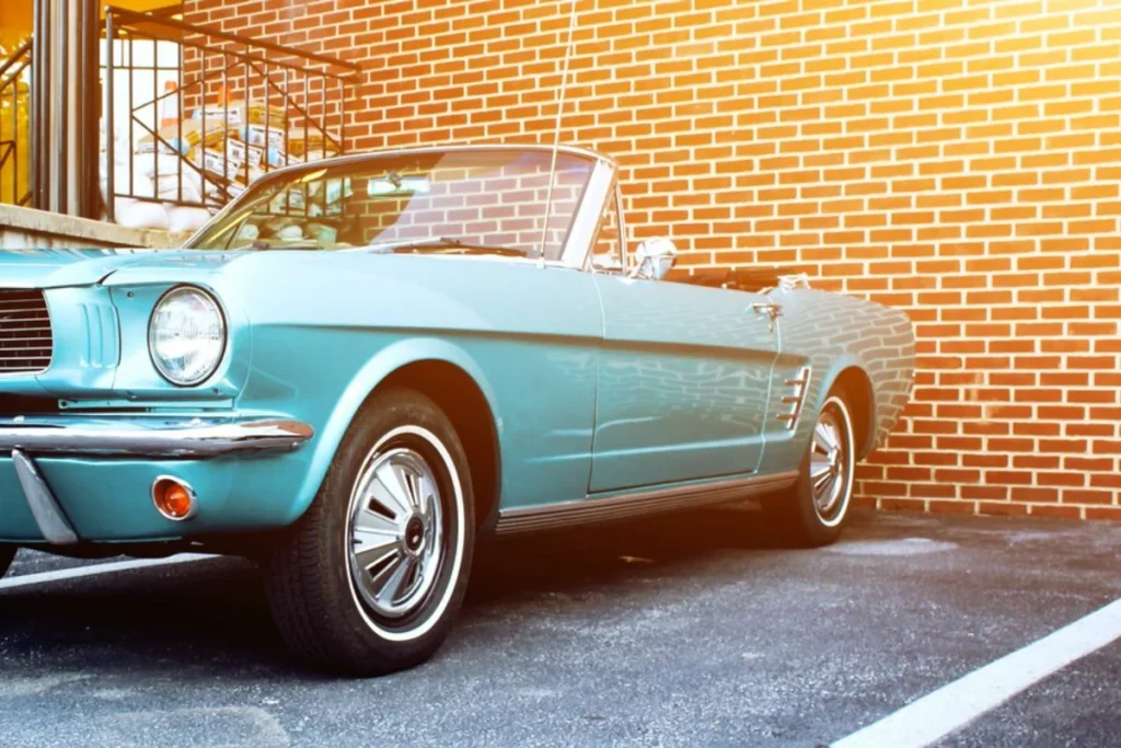 Vintage turquoise convertible car parked in front of a brick wall.