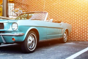 Vintage turquoise convertible car parked in front of a brick wall.