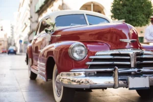 A beautifully restored vintage red car, decorated with white ribbons, parked on a sunlit street