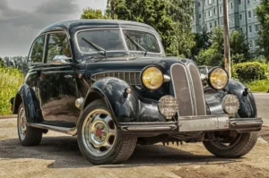 A vintage black car with distinctive round headlights and chrome grille, parked on a street