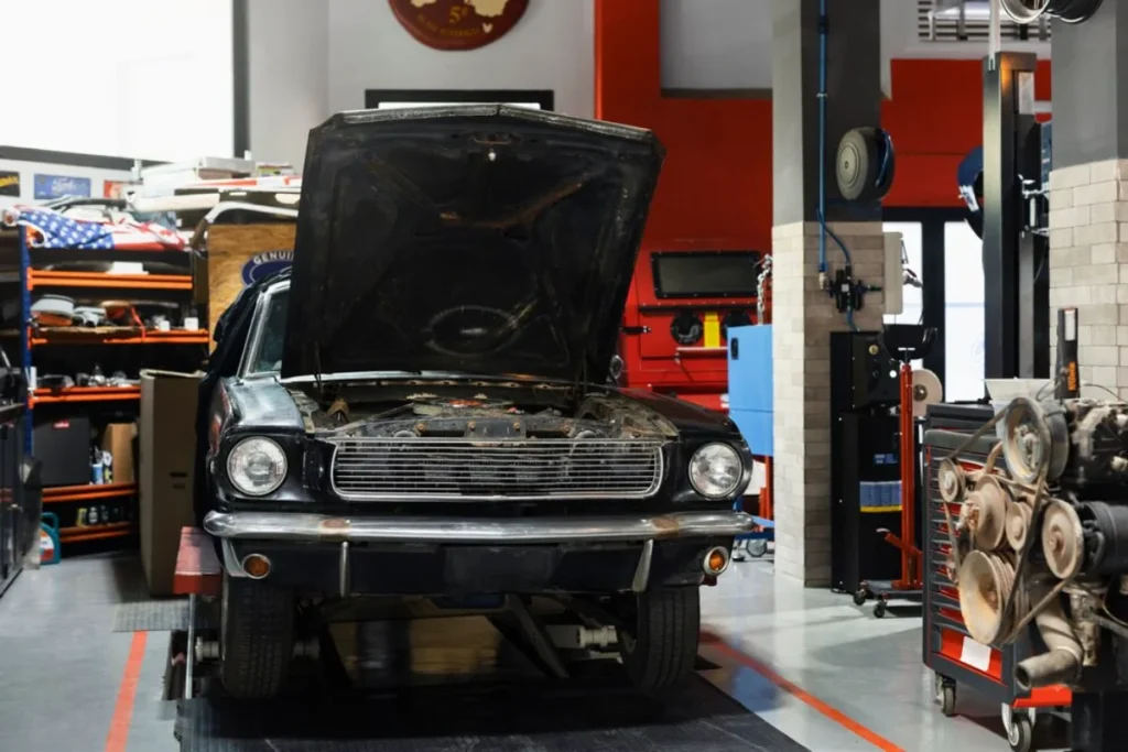 A vintage car with an open bonnet undergoing maintenance