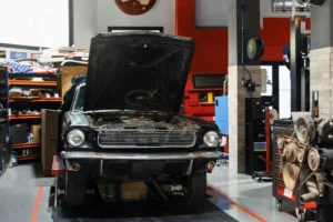 A vintage car with an open bonnet undergoing maintenance