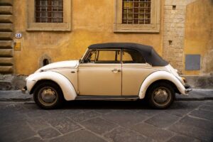 Vintage cream-colored convertible car parked beside a yellow stucco wall on a cobblestone street.