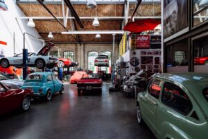 Vintage cars displayed inside a spacious, industrial-style garage with large windows and automotive memorabilia.