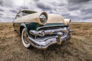 Classic green and cream car with circular headlights, parked in a grassy field under a cloudy sky.